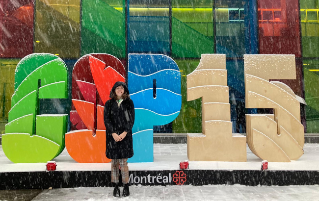 Image of Danielle standing infront of a COP15 sign whilst it is snowing.