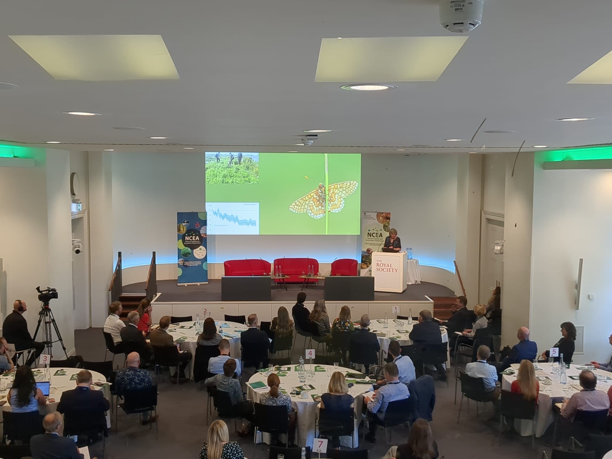 An overhead shot of guests at the NCEA stakeholder showcase. Guests are looking at at a presentation on 'why monitoring matters' being delivered by Rosie Hails, from the National Trust.