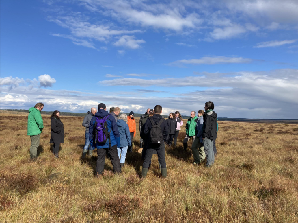 workers are on a peatland in the forefront of the image, behind blue skies with a few clouds