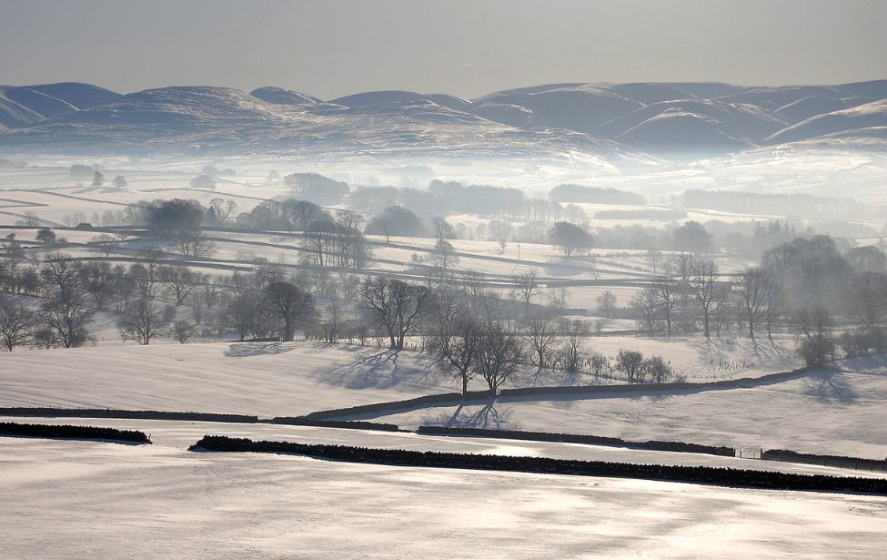 View of rolling hills covered with snow and mist.